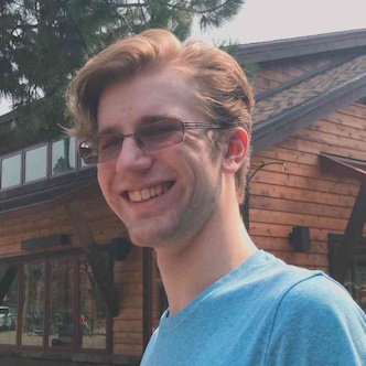 A smiling, upbeat picture of me in a blue shirt. I'm traveling, and the picture background is a smaller town center the pacific northwest.